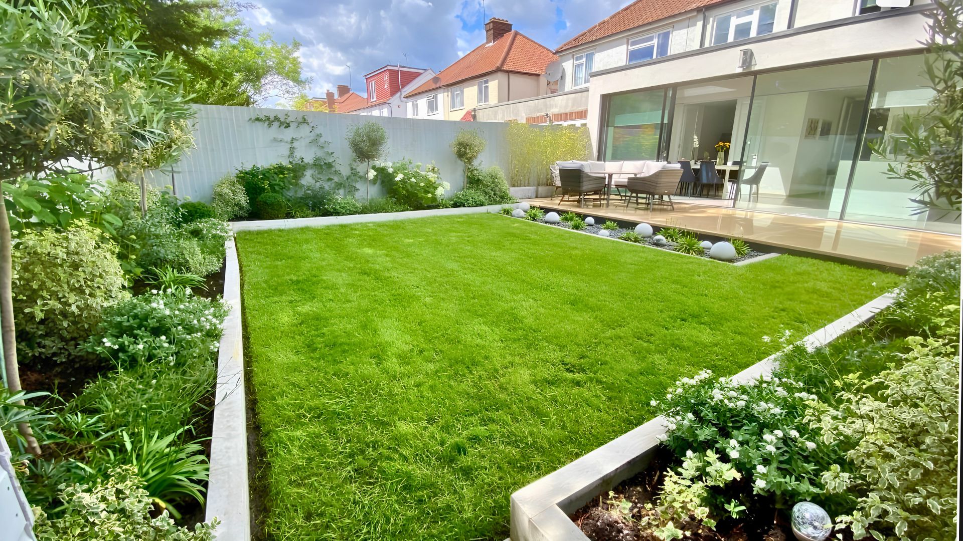 Contemporary white garden design in Wembley, London — rear garden with porcelain patio and lawn